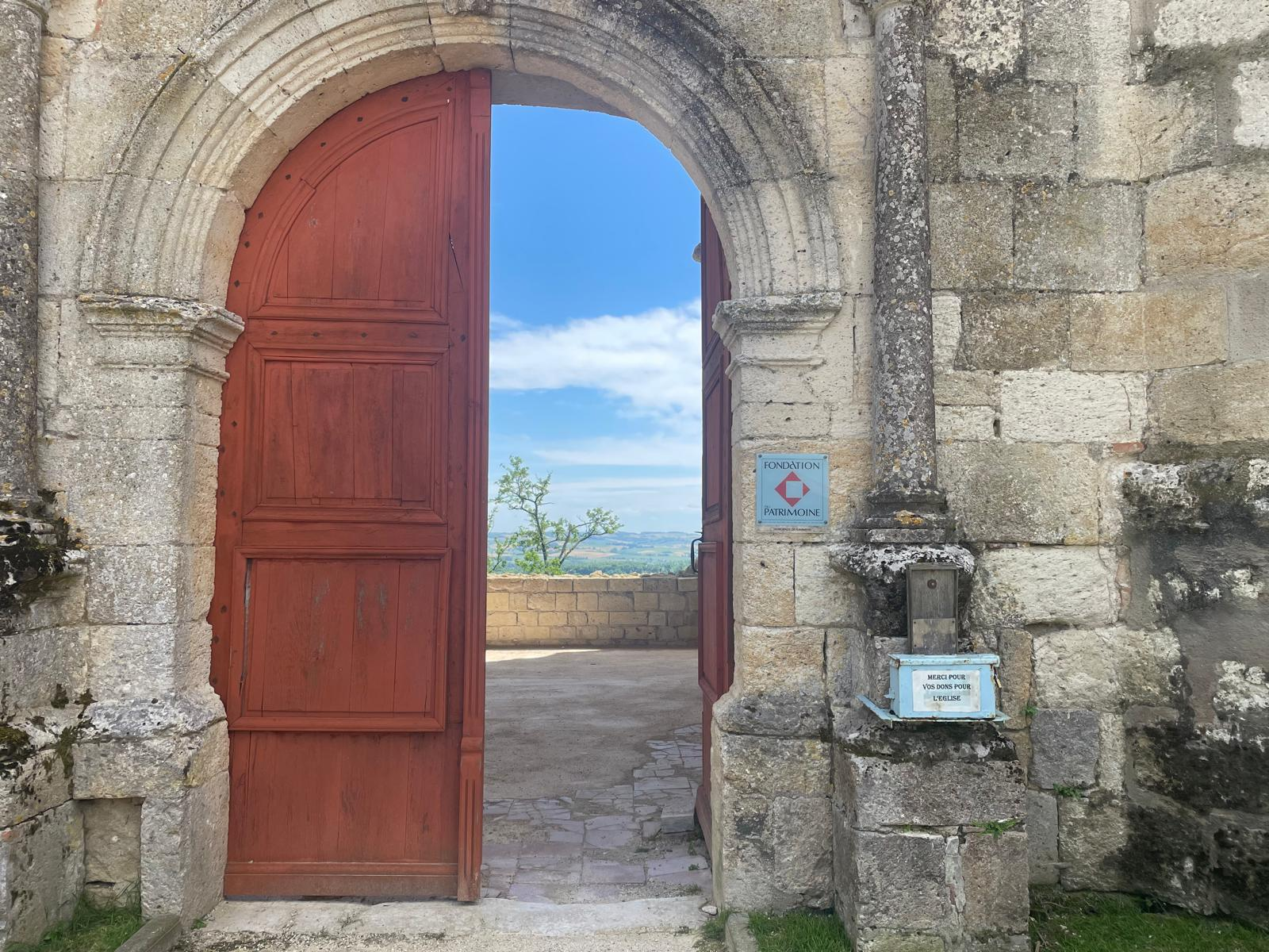 Porte rouge ouverte sur le paysage au château de Flamarens